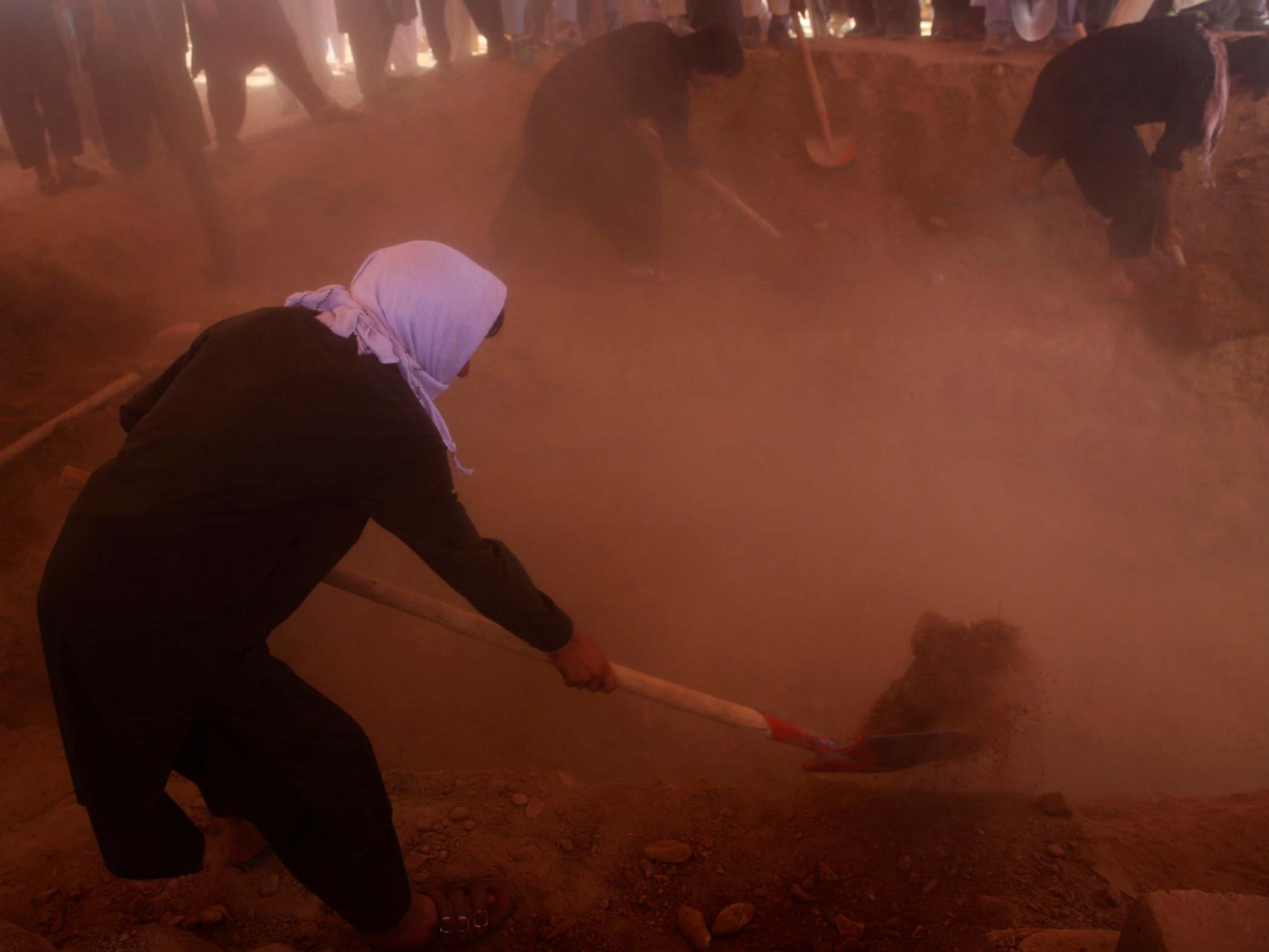 Afghans fill the graves of victims of the Dubai City wedding hall bombing during a mass funeral in Kabul