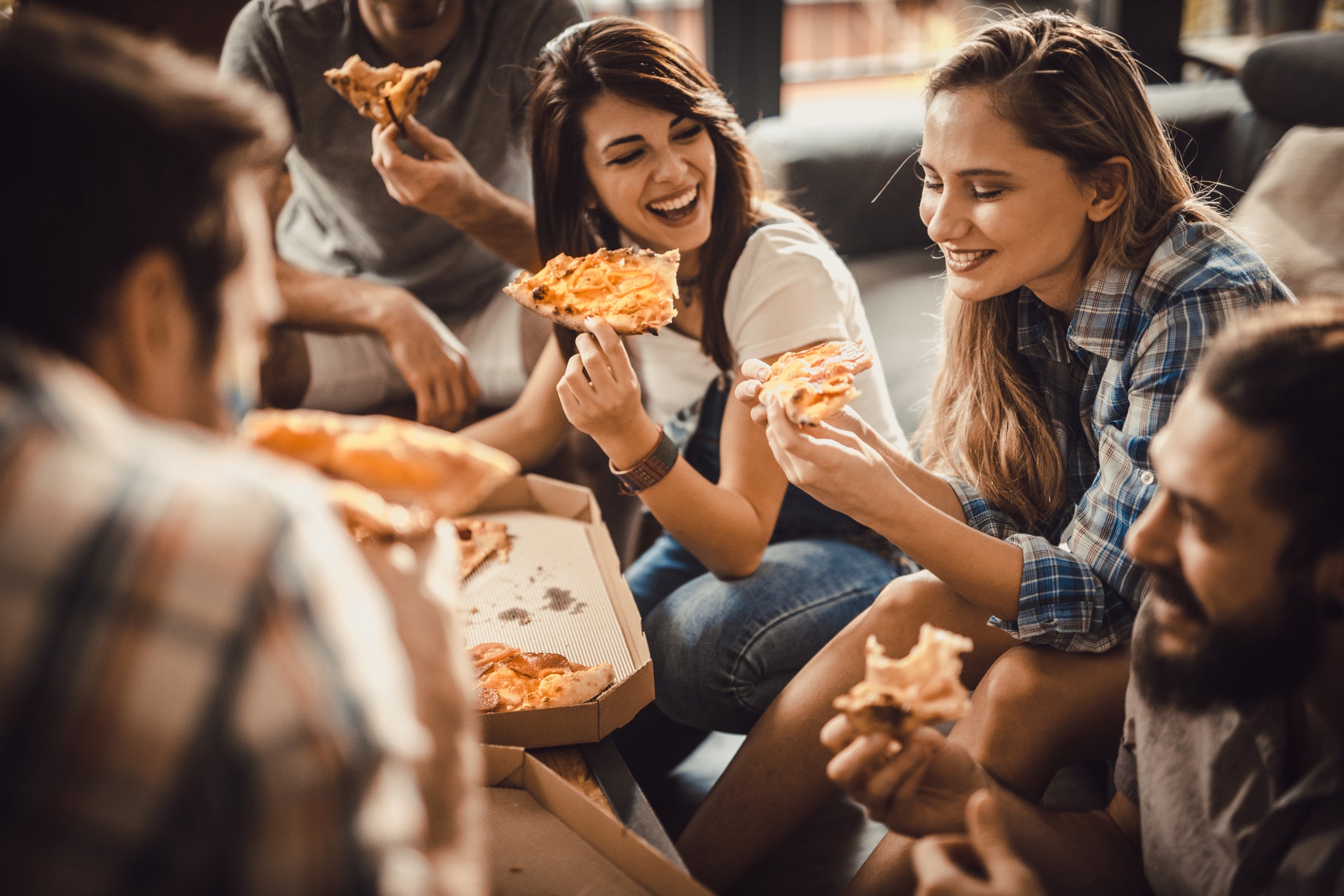 Young happy friends having fun while eating pizza at home