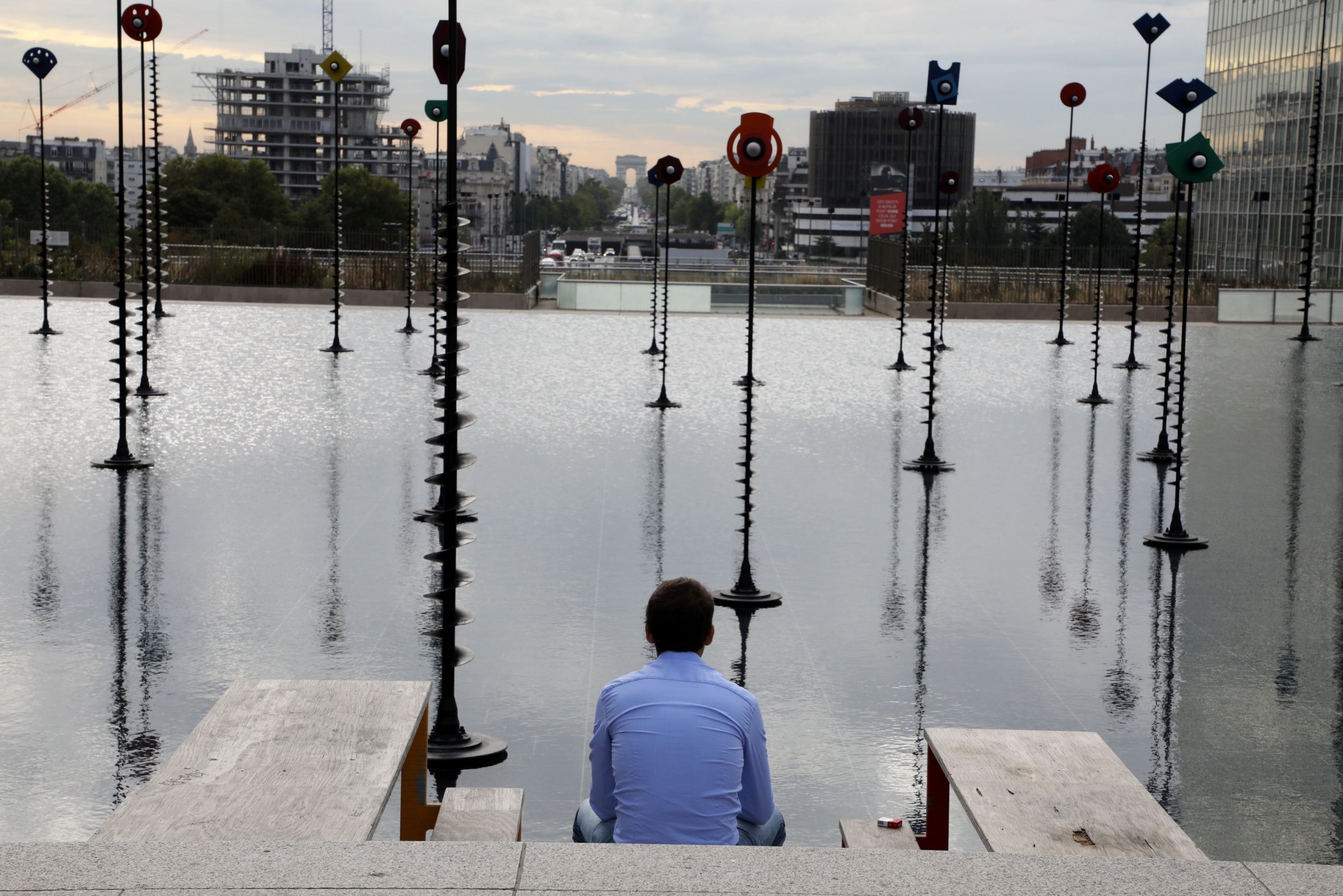 A man looks towards the Arc de Triomphe in Paris from a Takis art installation titled ‘Le Bassin’