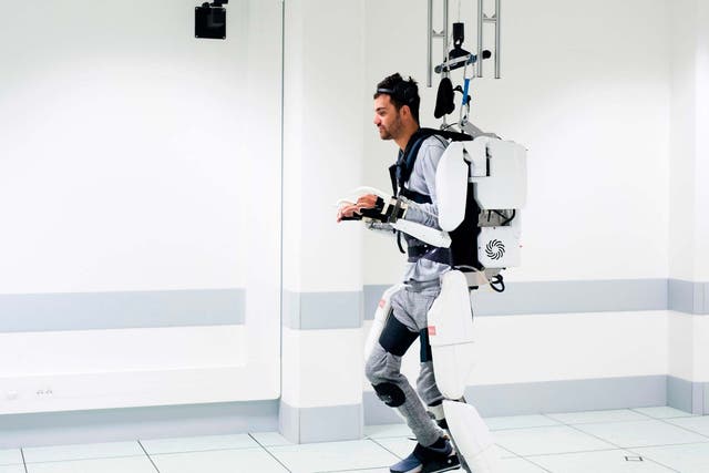 Thibault walks in the robotic suit using a harness for balance
