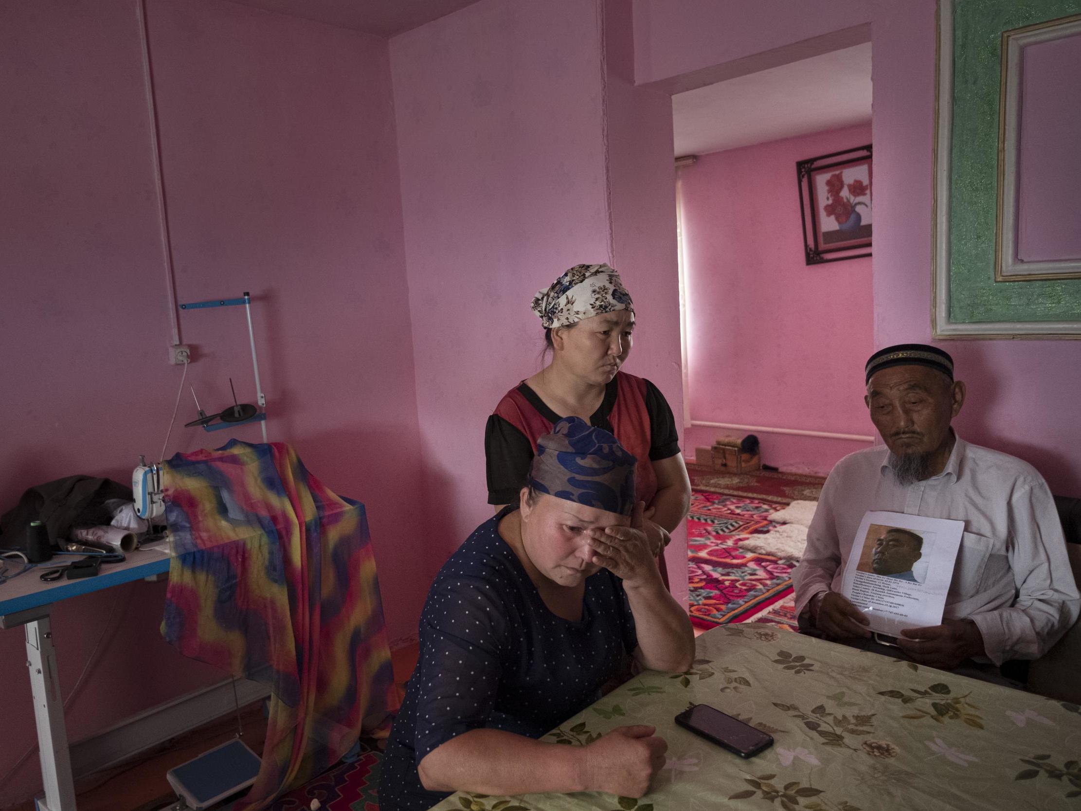 Auelkhan (centre) visits with Gulnar Kosdaulet (left), and Akbar Yenkelesh in their home in Akshi. Kosdaulet's husband, Sarsenbek Akbar, is in a camp in Xinjiang. Yenkelesh, her father-in-law, holds up a photo of his son.