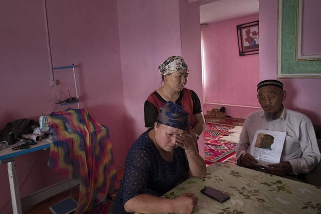 Auelkhan (centre) visits with Gulnar Kosdaulet (left), and Akbar Yenkelesh in their home in Akshi. Kosdaulet's husband, Sarsenbek Akbar, is in a camp in Xinjiang. Yenkelesh, her father-in-law, holds up a photo of his son.