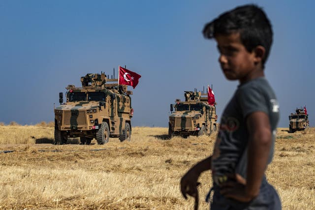 A Syrian boy watches as Turkish military vehicles, part of a US military convoy, take part in a joint patrol in the Syrian village on the outskirts of Tal Abyad town