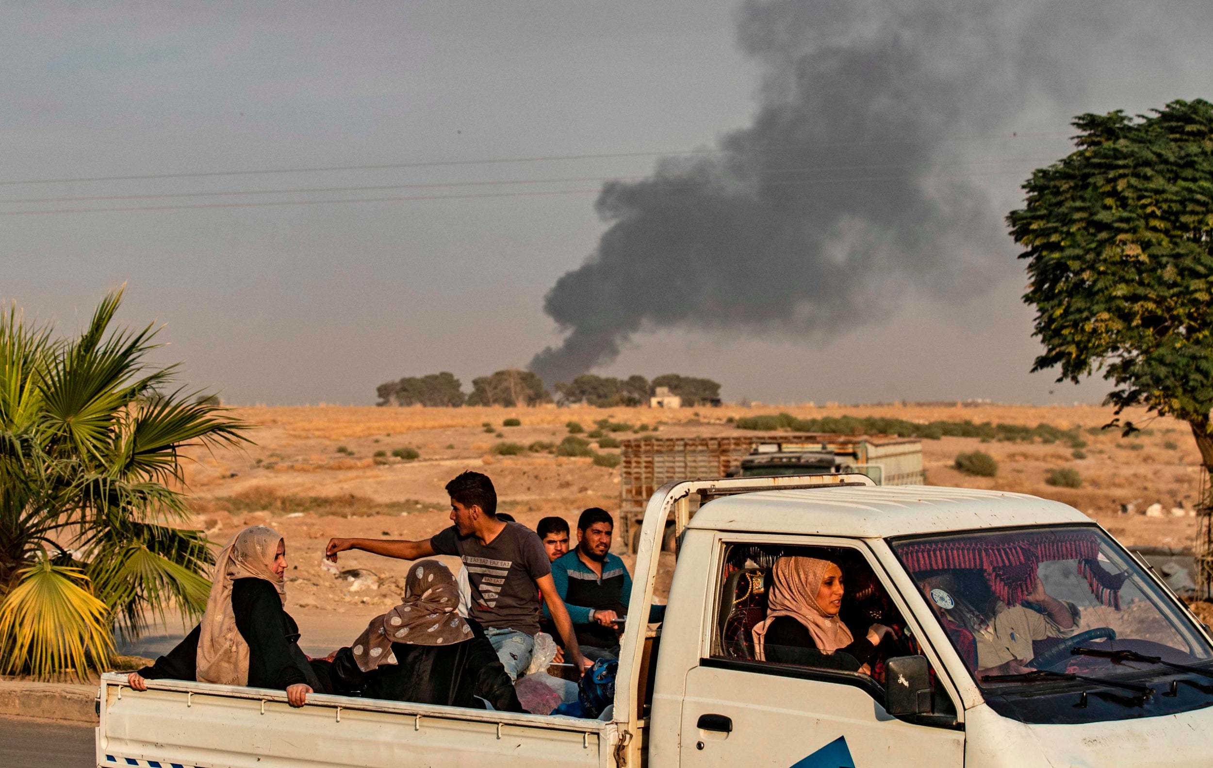 Civilians ride a pickup truck as smoke billows following Turkish bombardment in the northeastern town of Ras al-Ain (AFP/Getty)