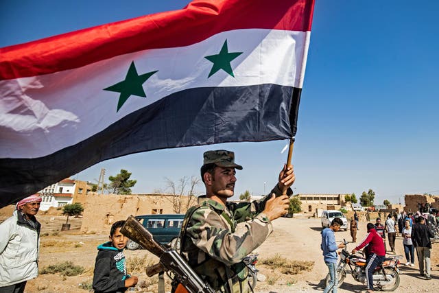 A Syrian regime soldier waves the national flag a street on the western entrance of the town of Tal Tamr in the countryside of Syria's northeastern Hasakeh province