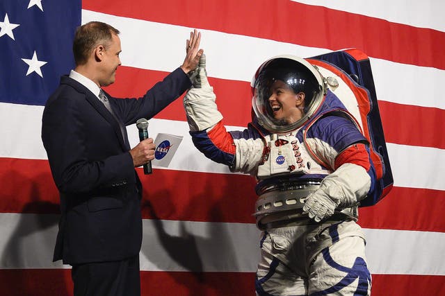 NASA administrator Jim Bridenstine (L) welcomes Advance space suit engineer, Kristine Davis (R), to the stage during a press conference displaying the next generation of space suits as parts of the Artemis program in Washington, DC