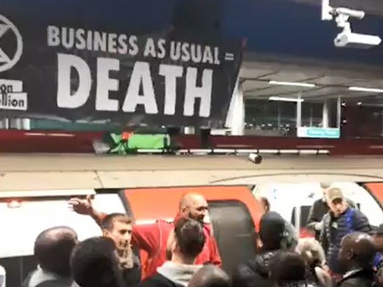 Extinction Rebellion protesters on the roof of an Underground train surrounded by angry commuters at Canning Town station in east London