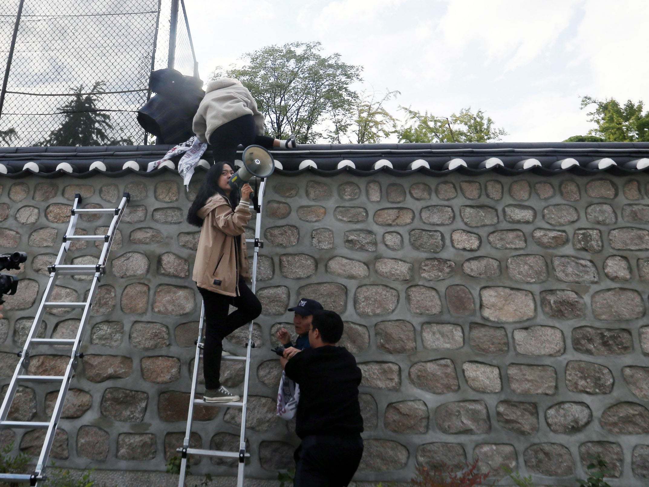 South Korean university student protesters climb over a wall during a protest at the US ambassador's residence in Seoul