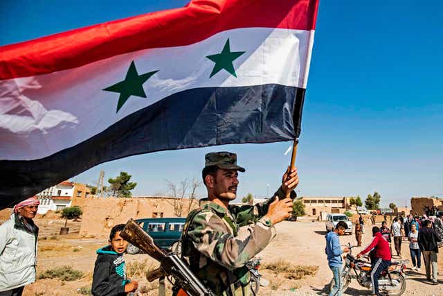 A Syrian regime soldier waves the national flag a street on the western entrance of the town of Tal Tamr in the countryside of Syria’s northeastern Hasakeh province on 14 October 2019