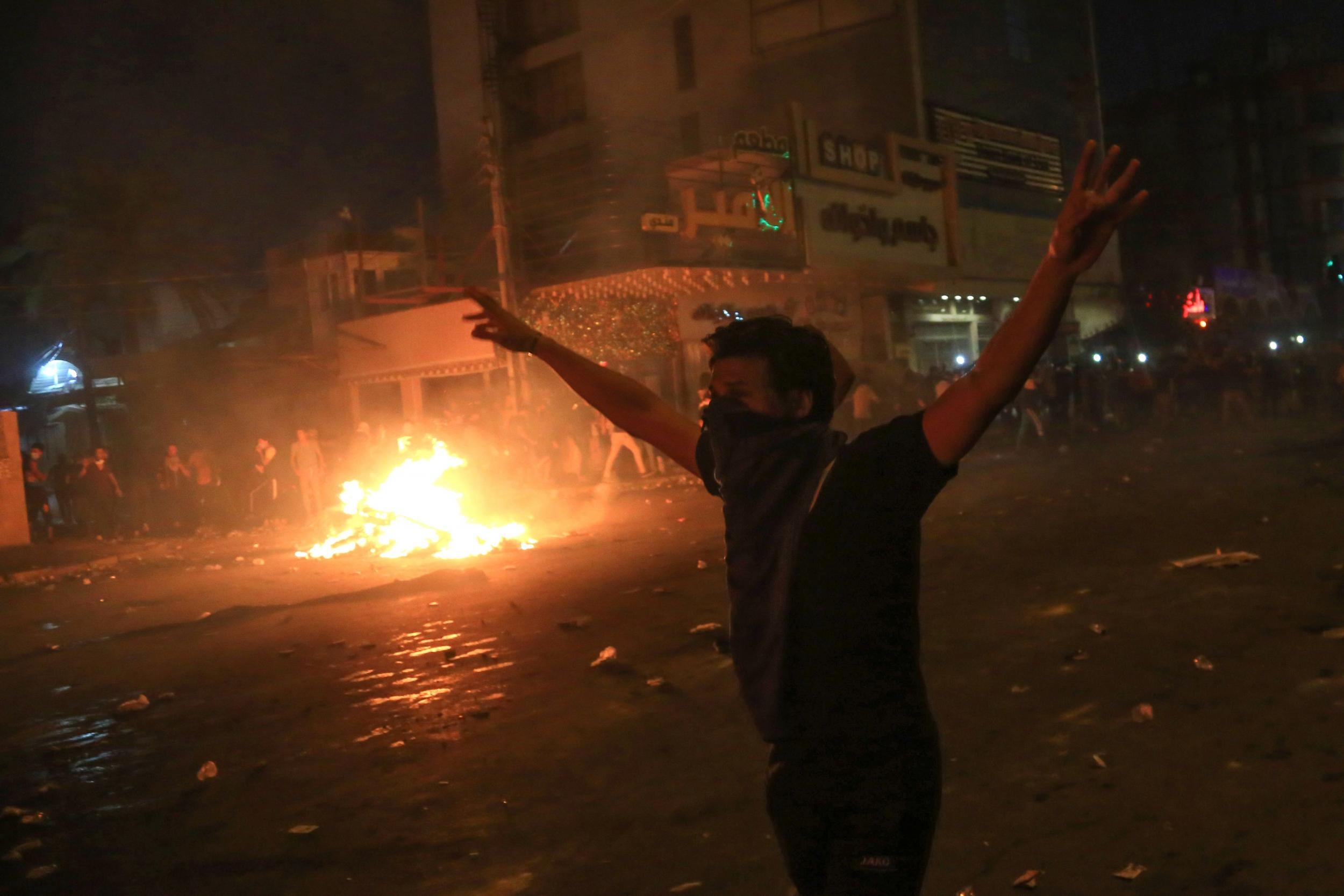 A protester gestures as burning tyres light up the night skies during anti-government protests in the Shiite shrine city of Karbala, south of Iraq's capital Baghdad,