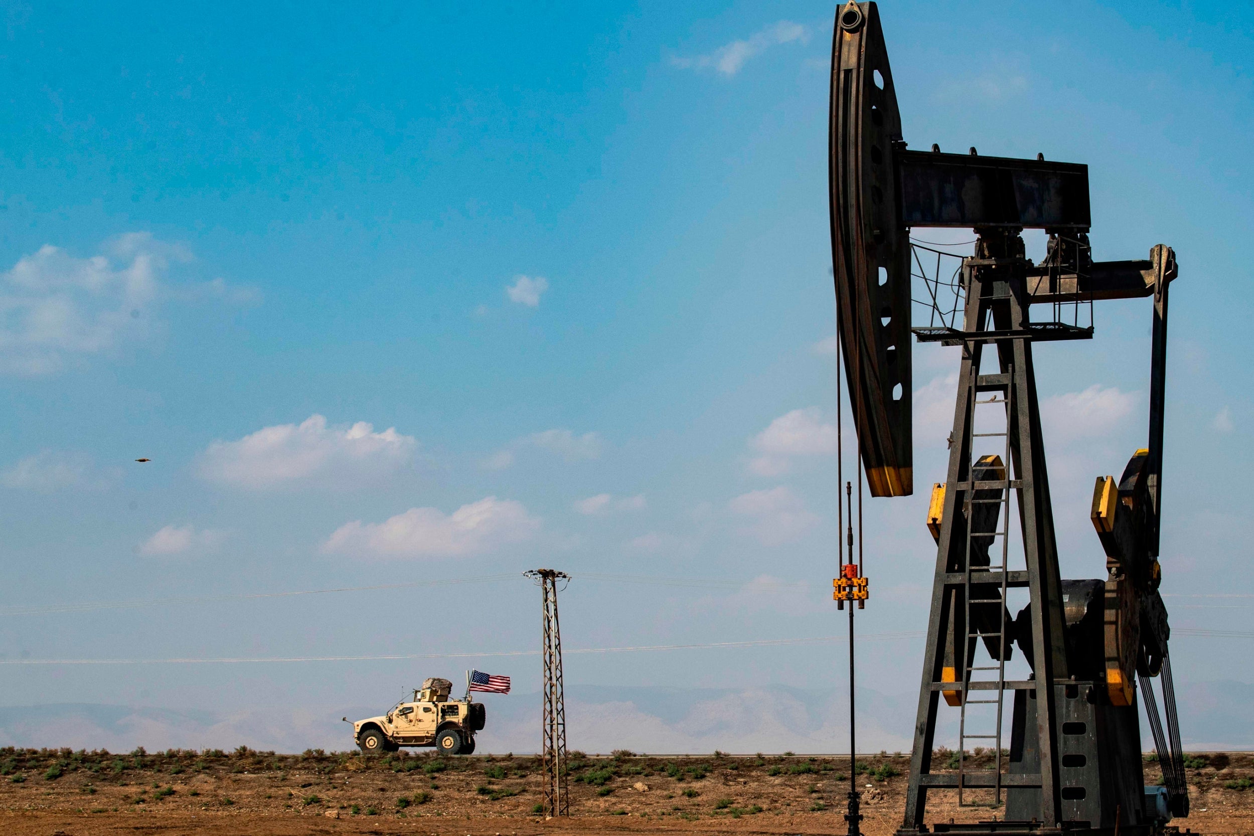 A US military vehicle drives past an oil pump jack in the countryside of Syria's northeastern city of Qamishli on 26 October