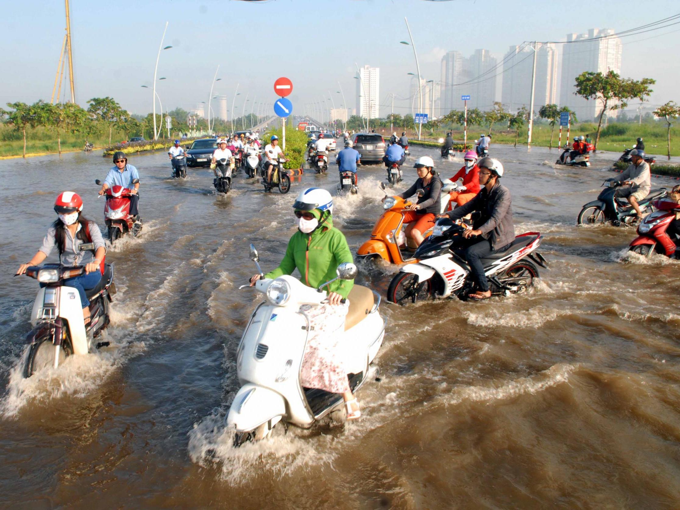 Cars and motorcycles drive on a road getting flooded due to high tide water and rain in Ho Chi Minh City in 2014