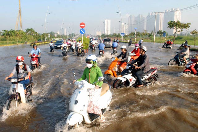 Cars and motorcycles drive on a road getting flooded due to high tide water and rain in Ho Chi Minh City in 2014