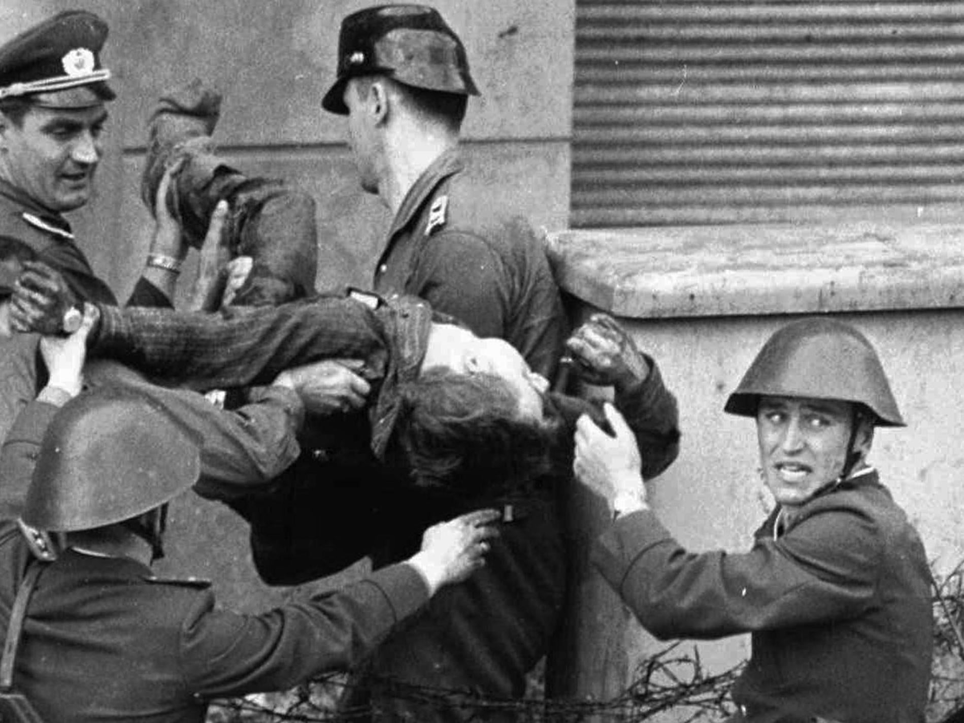 A bloodied and dying Fechter is carried away by the East German guards who shot him down as he tried to flee to the west