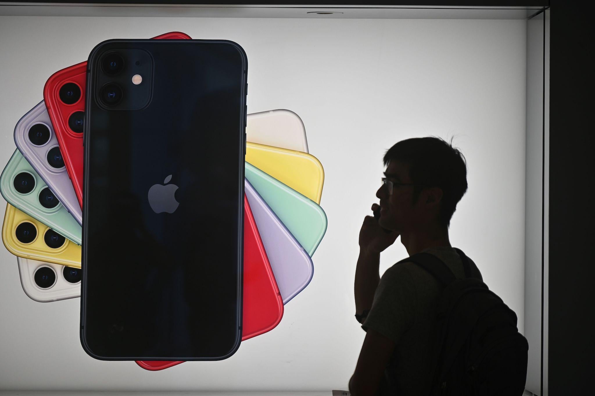 A man uses his mobile phone as he walks past advertising for the new iPhones outside the Apple store in Hong Kong on October 10, 2019