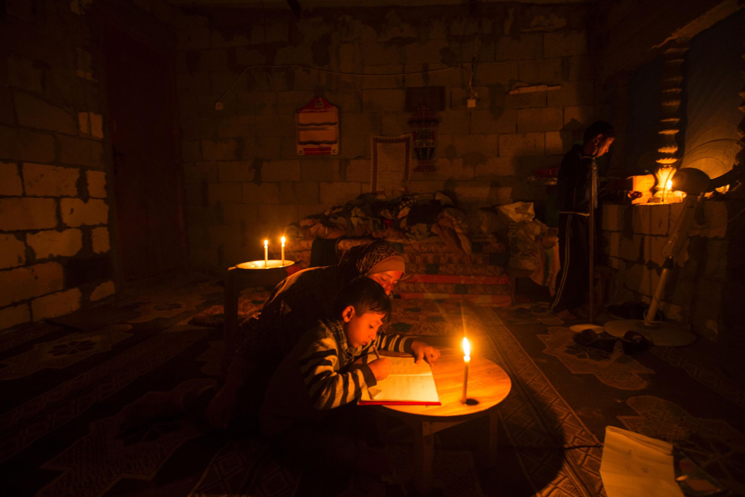 A Palestinian woman helps her son study, by candlelight, at their makeshift home in the Khan Yunis refugee camp in the southern Gaza Strip