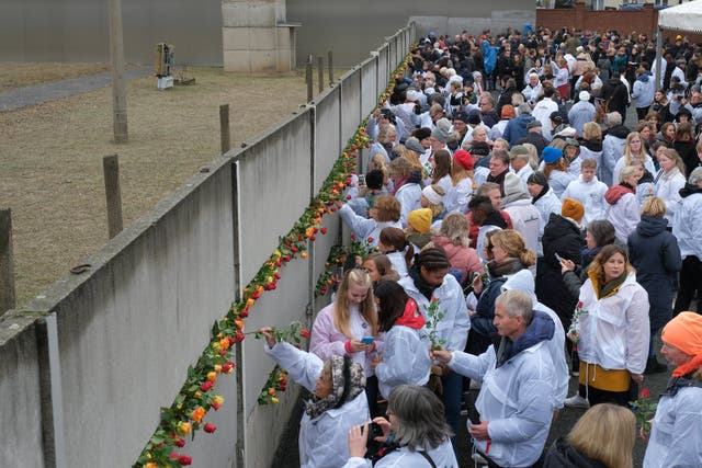People stick flowers into slats of a still-standing portion of the Berlin Wall at Bernauer Strasse following a ceremony to celebrate the 30th anniversary of the fall of the Berlin Wall