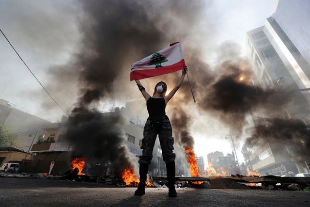 Anti-government protester holds a Lebanese flag while standing in front burning tires that block a road in the town of Jal el-Dib, north of Beirut