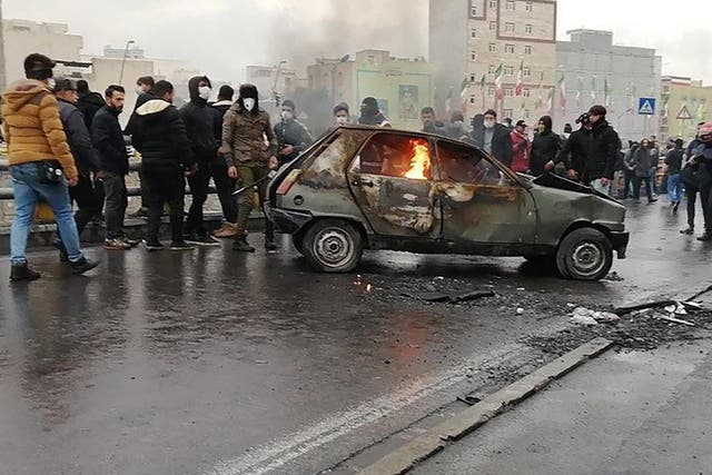 Protesters in Iran gather around burning car during a demonstration against rise in petrol prices