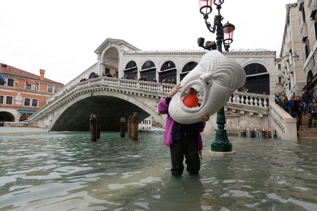 A tourist holds a huge mask amid rising water levels in Venice on 17 November