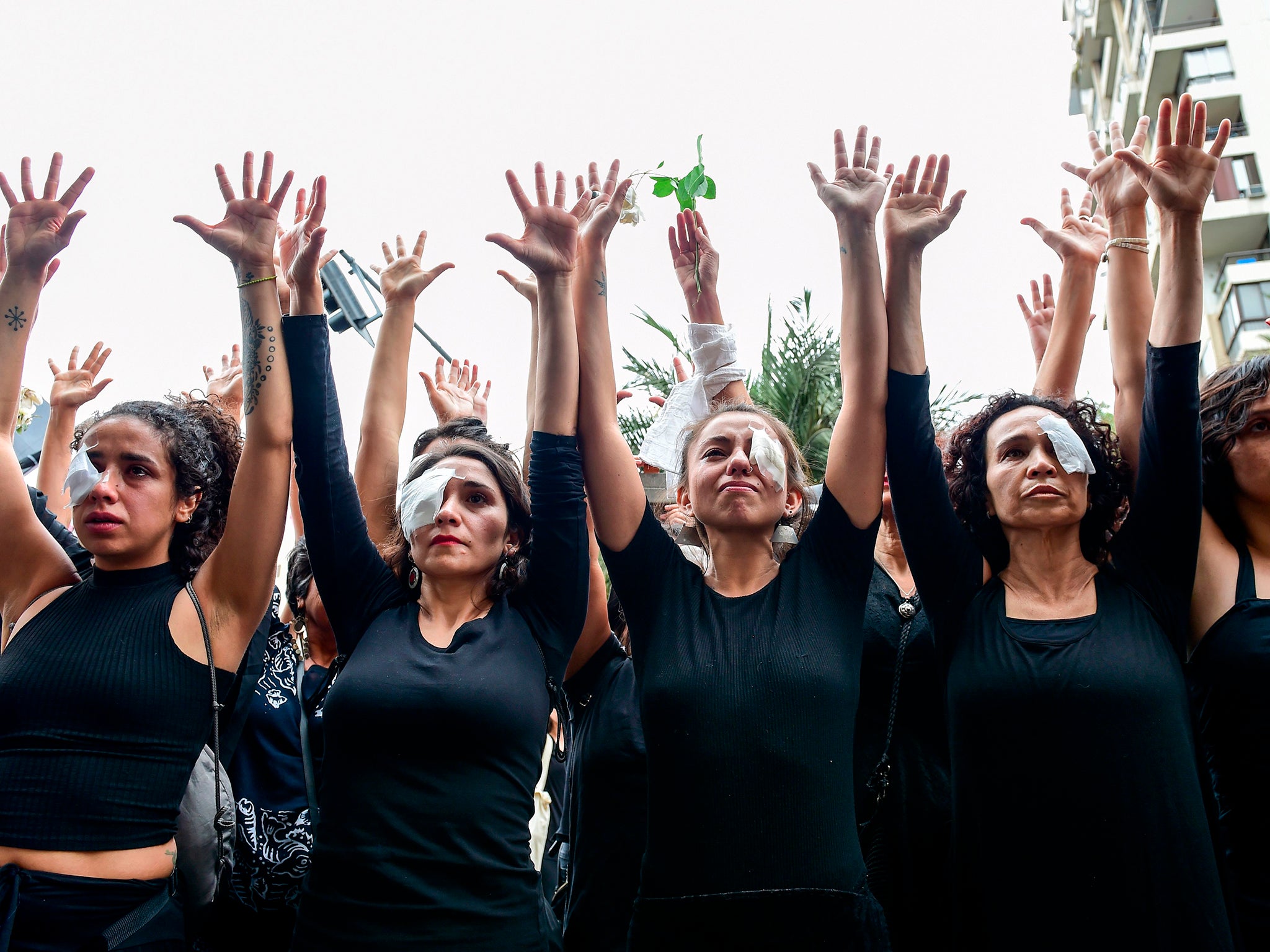 Women dressed in black and wearing eye patches, representing protesters injured with pellets shot by riot police