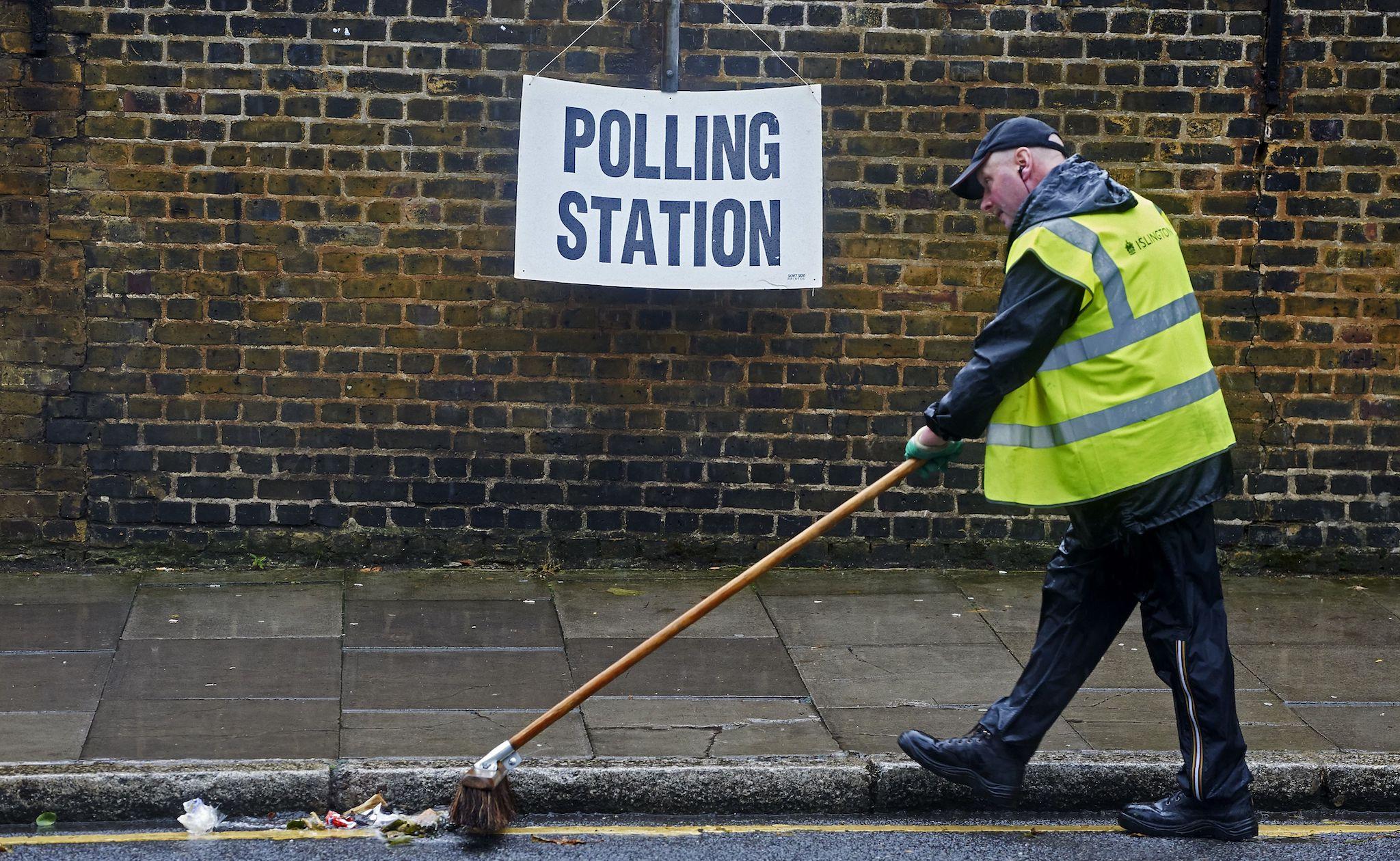 A worker sweeps rubbish in the raod near a polling station sign in London on June 23, 2016, as Britain holds a referendum on wether to stay in, or to leave the European Union