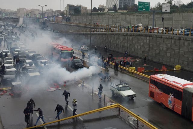 Riot police try to disperse people as they protest on a highway against increased gas prices in Tehran