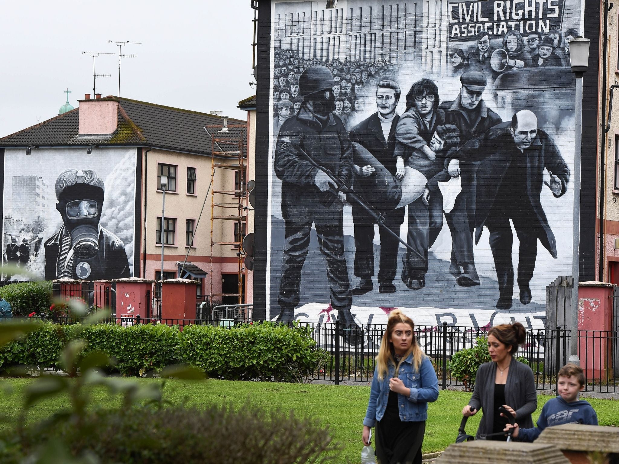 A family walks past a mural in Derry depicting a scene from Bloody Sunday