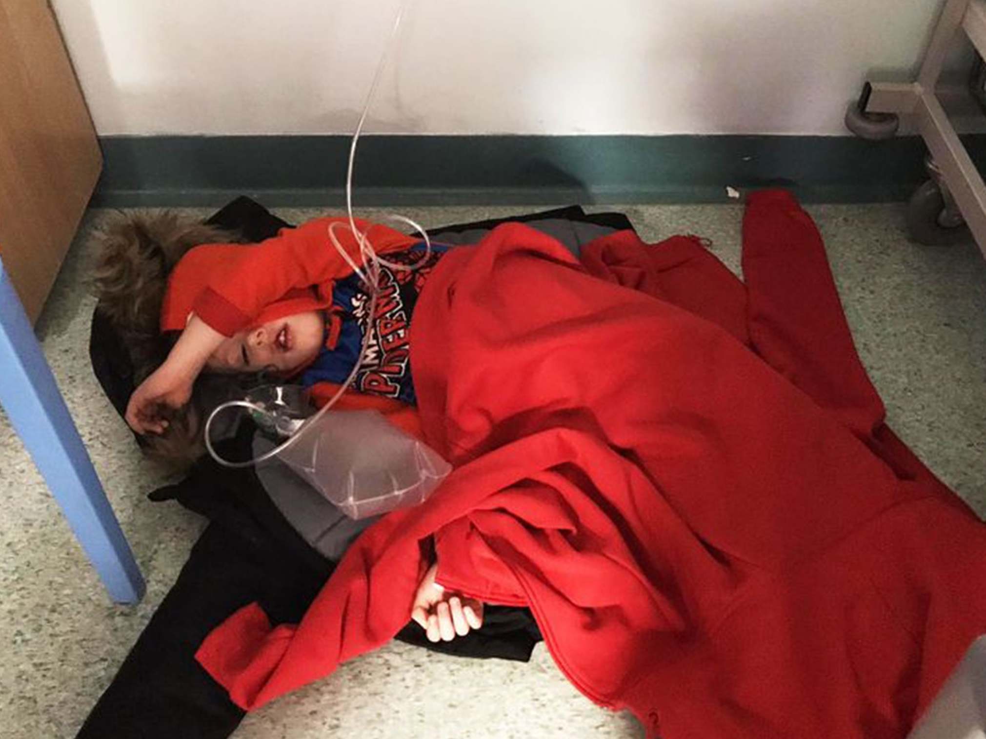 Four-year-old Jack Williment is covered in coats on the floor at Leeds General Infirmary due to a lack of beds.