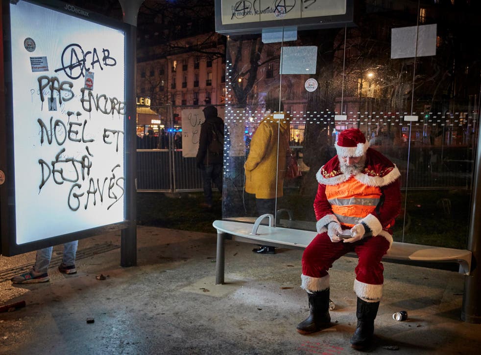 A protester dressed as Santa in a Paris bus shelter with graffiti that reads 'Not yet Christmas and already stuffed' on 17 December