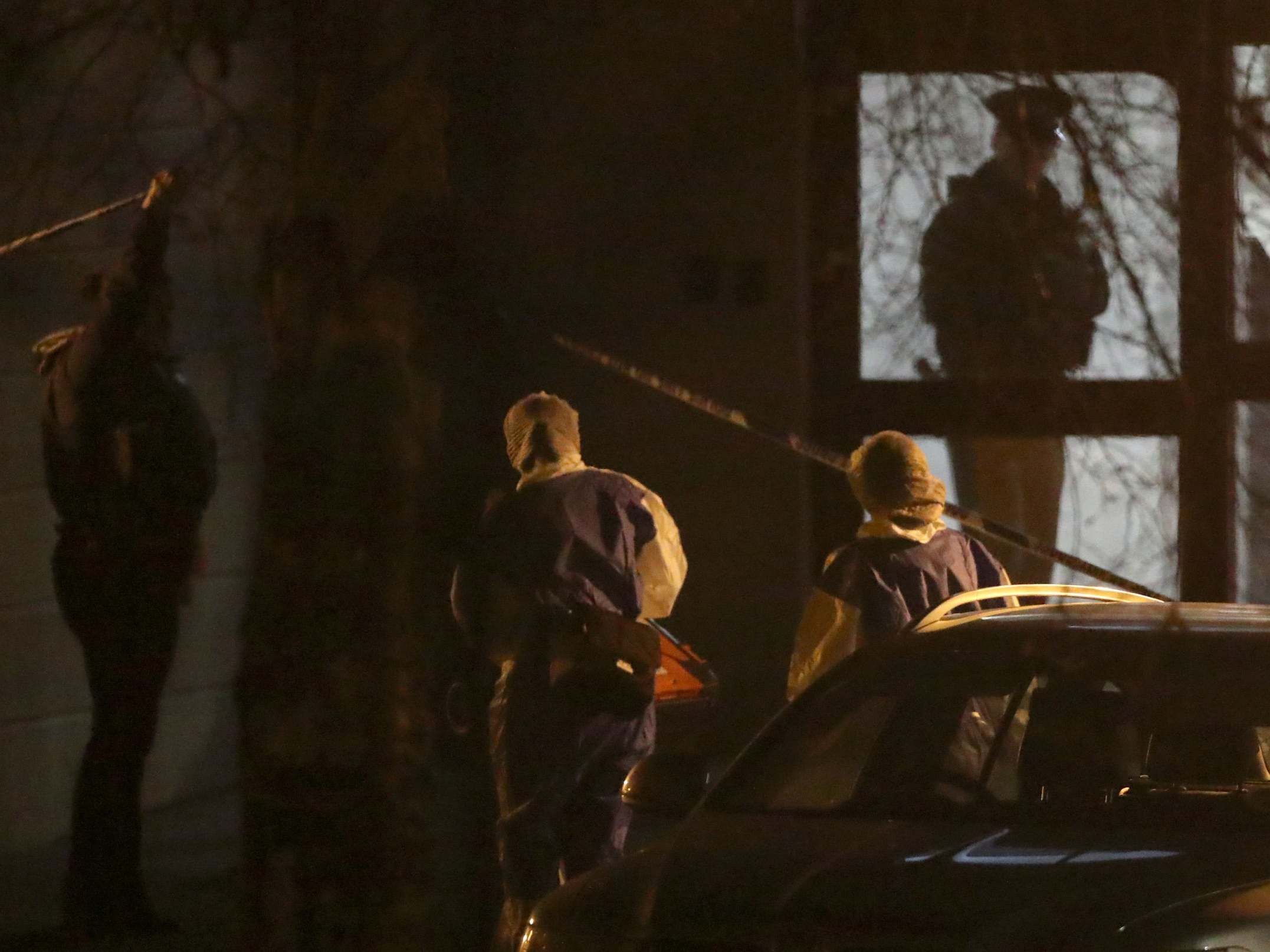 A police officer lifts the cordon tape for forensic officers as they enter a building on Kinnaird Close in Belfast, after the bodies of a man and a woman were found in an apartment