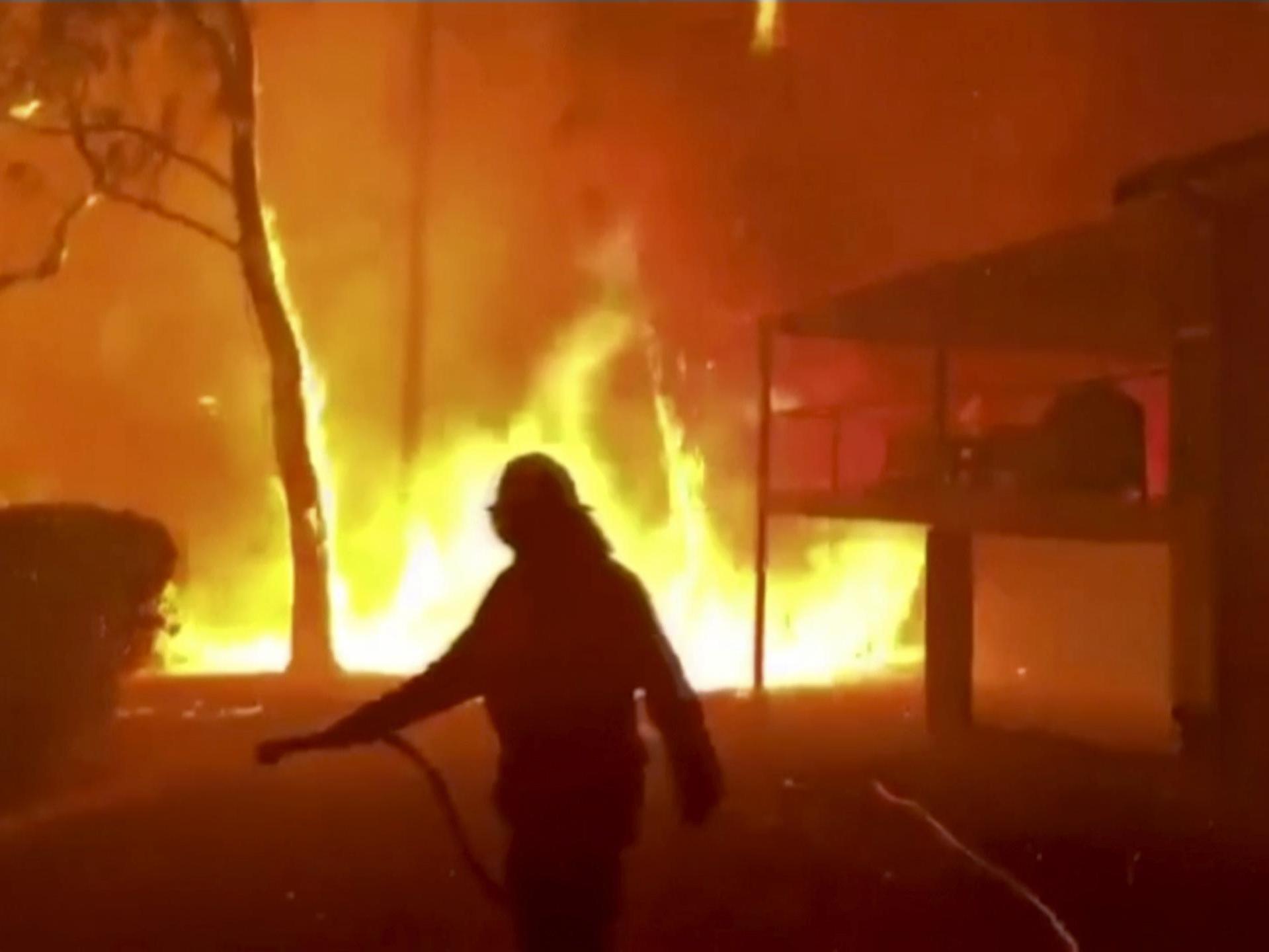 A firefighter sprays water on a fire moving closer to a home in Blackheath, New South Wales state