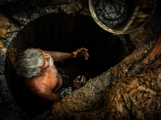 Kaverappa. a manual scavenger in Bangalore, passes a bucket out of a pit. He wants to leave the job behind but feels there is no alternative