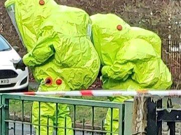 Two emergency responders in hazmat suits attend to a man believed to have ingested poison