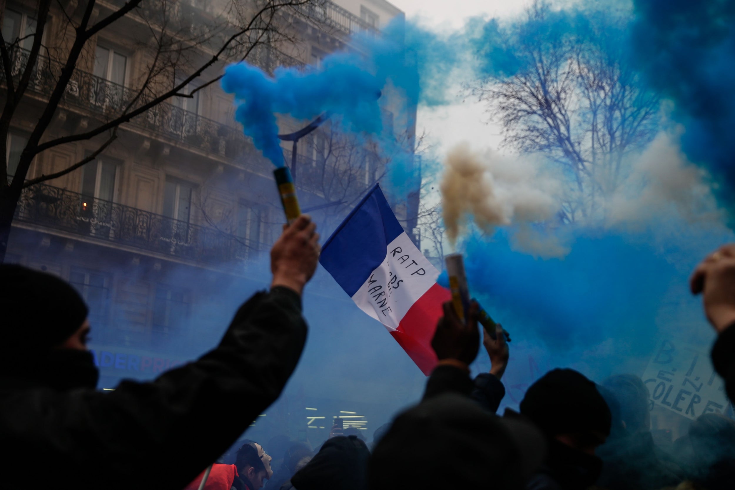 Protesters burn blue flares and wave flags during a demonstration in Paris