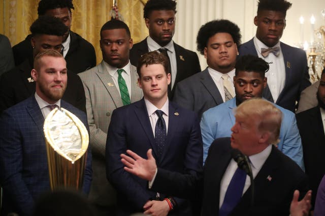 Members of the LSU Tigers look on as Donald Trump makes jokes at a reception for them in the East Room of the White House to reward their victory in the college football playoff final