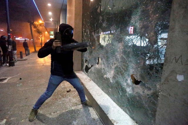 A protester smashes the window of a bank as demonstrations against the government continue in Beirut