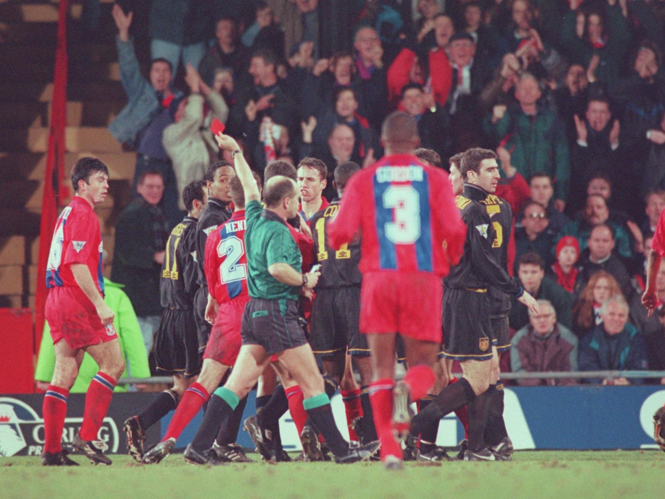 Eric Cantona is led off the pitch after fighting with a fan at Selhurst Park in January 1995