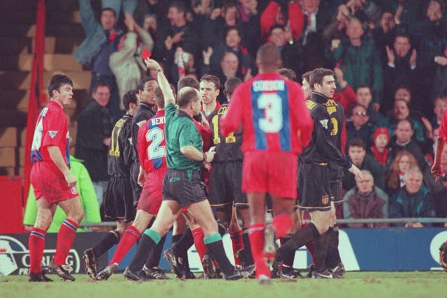 Eric Cantona is led off the pitch after fighting with a fan at Selhurst Park in January 1995
