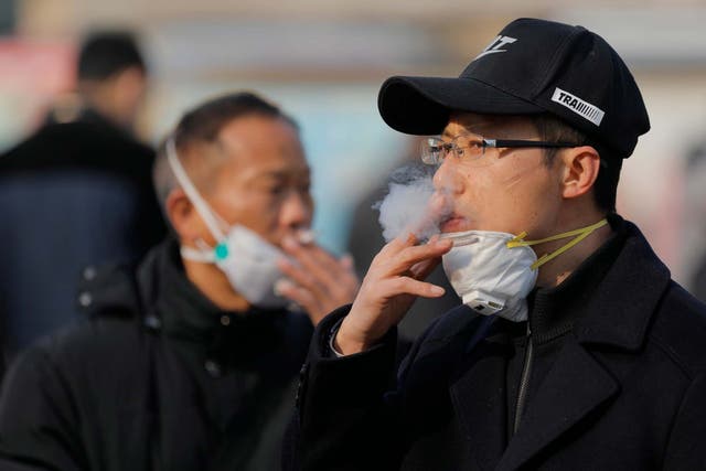Chinese passengers pull down their masks while smoking at the Beijing railway station