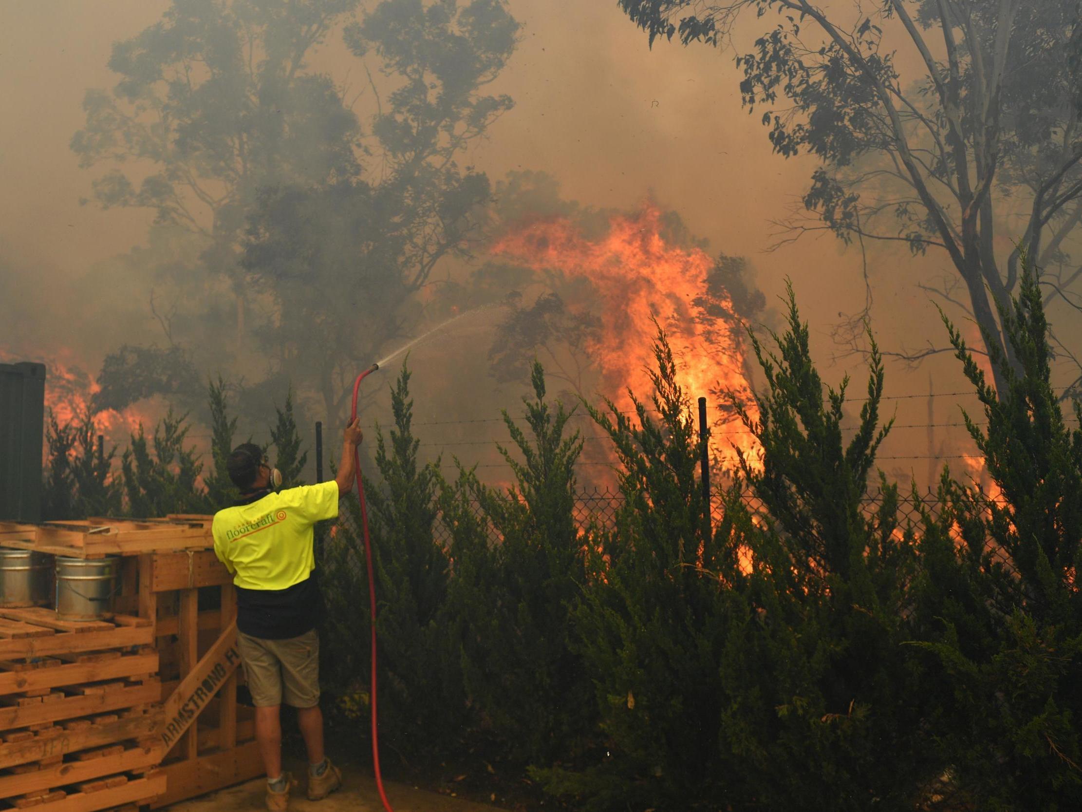 A worker tries to put out a bushfire behind a row of factories near West Queanbeyan (Reuters)