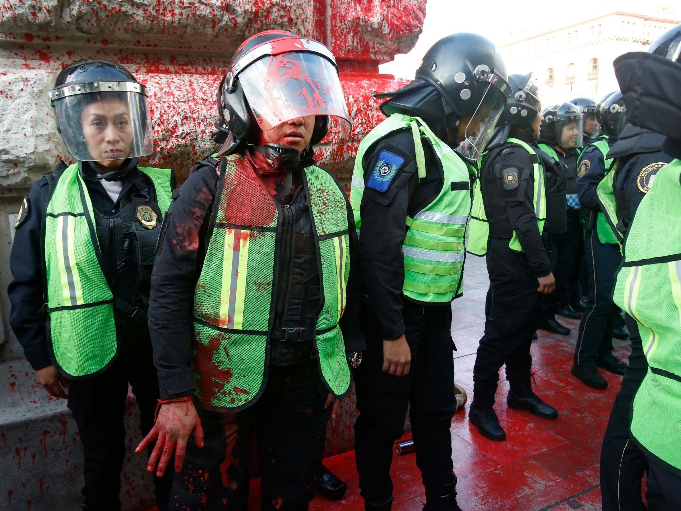 A female police officer covered in red paint stands by during a protest against the deaths of two women in Mexico City