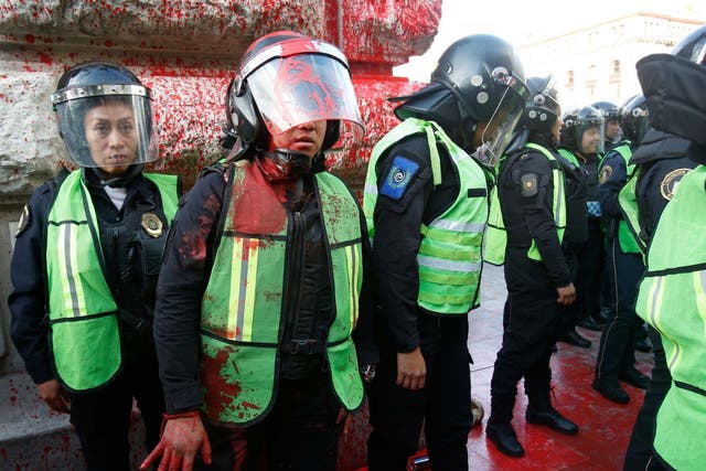 A female police officer covered in red paint stands by during a protest against the deaths of two women in Mexico City