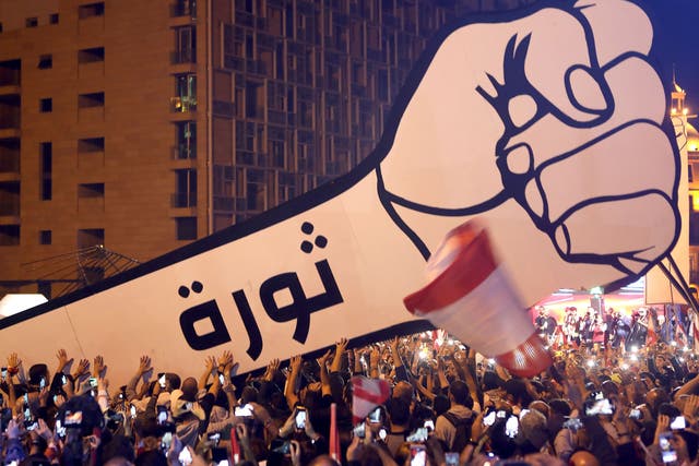 Lebanese protesters raise a giant fist that bears the Arabic word revolution