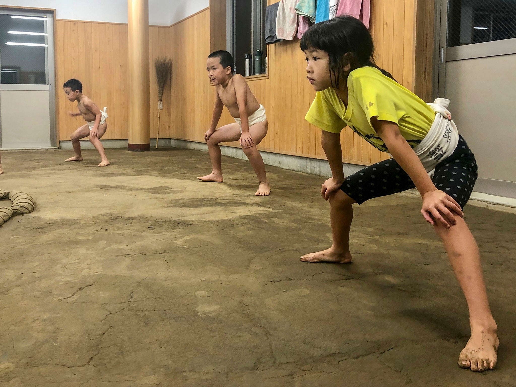 Himeka Suzuki, seven, begins a sumo practice session with a shiko exercise, slowly stomping her feet, alongside her fellow classmates. Each student must complete 100 stomps to warm up