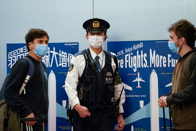 Foreign tourists walks toward a Japanese police officer at an arrival gate in Tokyo International Airport