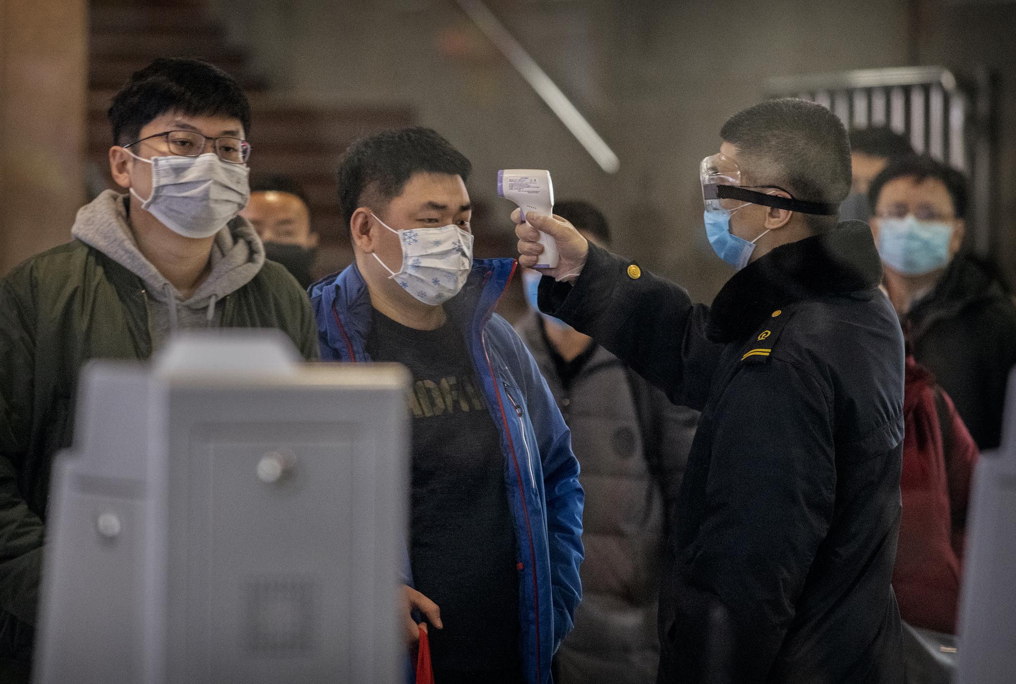 A Chinese passenger that just arrived on the last bullet train from Wuhan to Beijing is checked for a fever by a health worker at a Beijing railway station on January 23, 2020 in Beijing, China