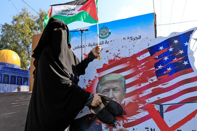 A Palestinian woman slams her shoes on a portrait of Trump during a demonstration in Gaza City