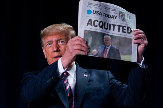 Donald Trump brandishes a newspaper with the banner headline "Acquitted" at the National Prayer Breakfast in Washington, a day after the Senate impeachment trial ended