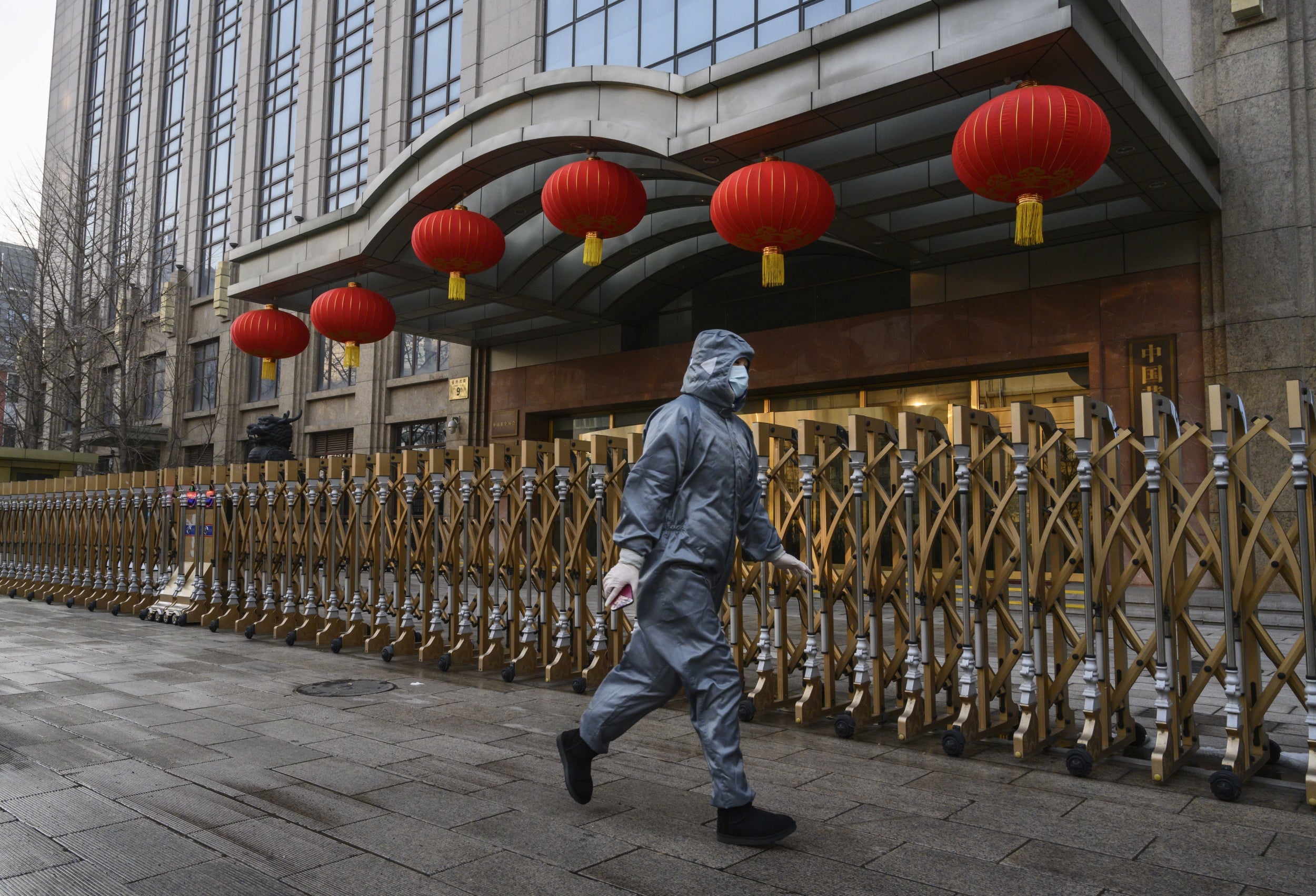 A woman wearing a protective suit and face mask walks past a closed building in Beijing